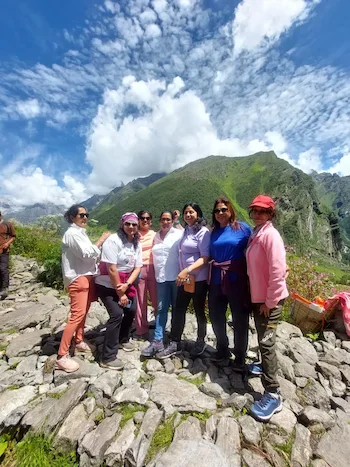 Trekking group standing on a rocky trail with lush mountains and blue skies in the Valley of Flowers.