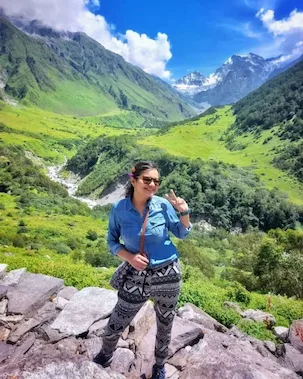 Trekker standing amidst the scenic greenery of the Valley of Flowers, surrounded by dramatic Himalayan landscapes.